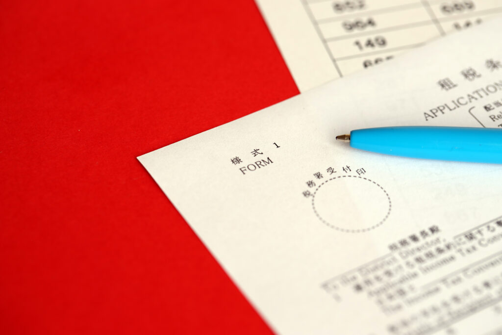 Dos documentos y un boligrafo de color azul sobre un fondo rojo representando traducción japonés