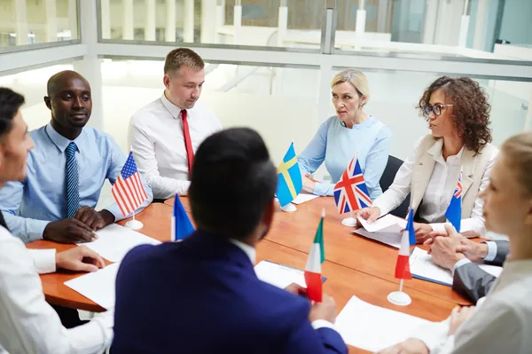 Grupo de hombres y mujeres sentados con banderas de diferentes países formados como traductores oficiales por e learning.