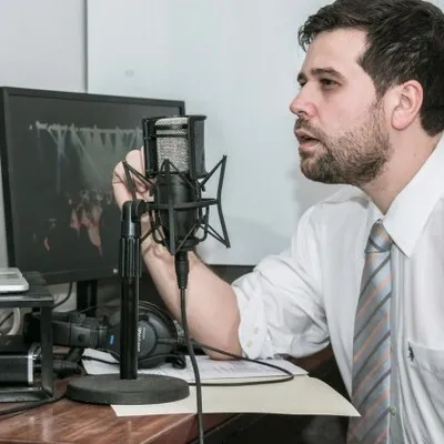 Fotografía de un hombre con camisa blanca y corbata hablando frente a un micrófono en una agencia de traducción.