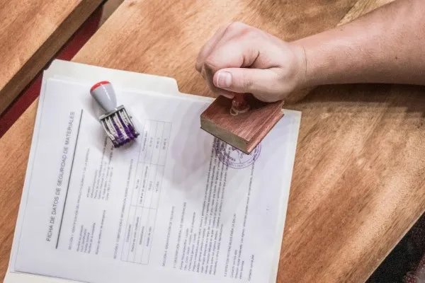 Fotografía de una persona colocando un sello en documentos oficiales sobre una mesa en una agencia de traducción.