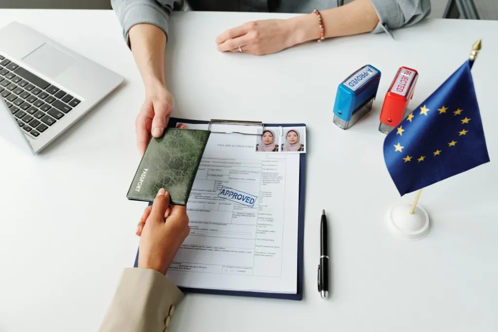 Traducción con IA: fotografía de una persona entregando documentos migratorios con fotografías a una autoridad.
