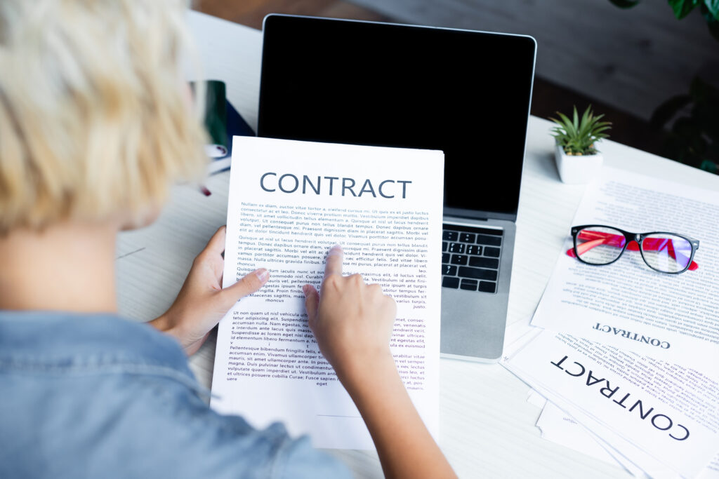 Traducción de contratos: Fotografía desde atrás de una mujer sosteniendo un documento que dice contrato.