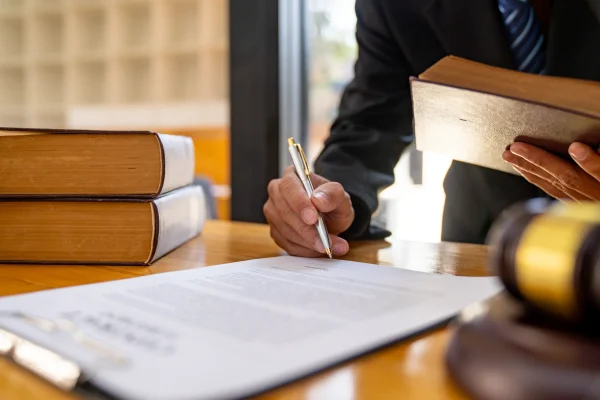 Un perito traductor Mérida firma un documento oficial en su escritorio, con libros de derecho y un mazo, validando una traducción.